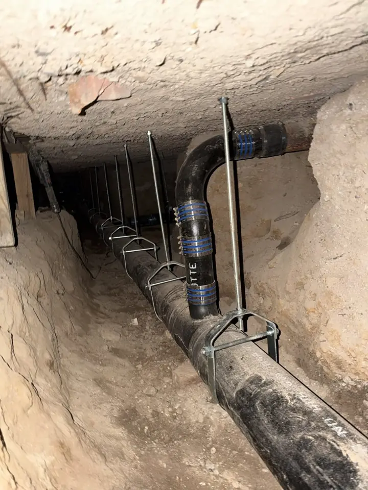 Hand-dug tunnel under a building with new no-hub cast iron drain line on clevis hangers