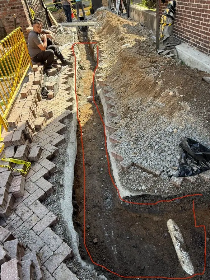 Trench dug through brick pavers toward a building for new electrical conduit